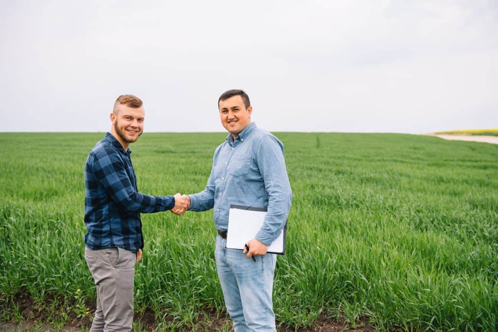 Farmers Hub farmers standing in a green wheat field and shake hands.